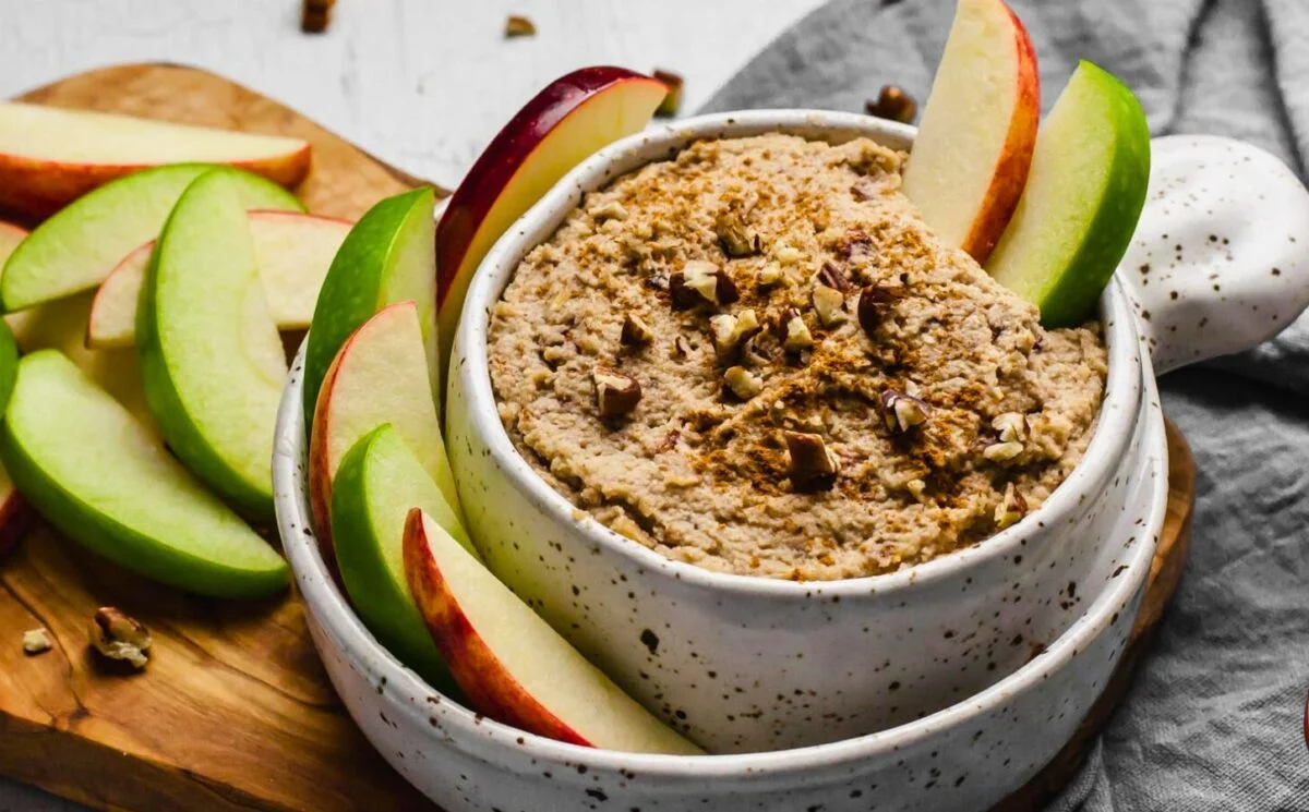 a bowl of creamy maple and toasted pecan dip with sliced apples on the side