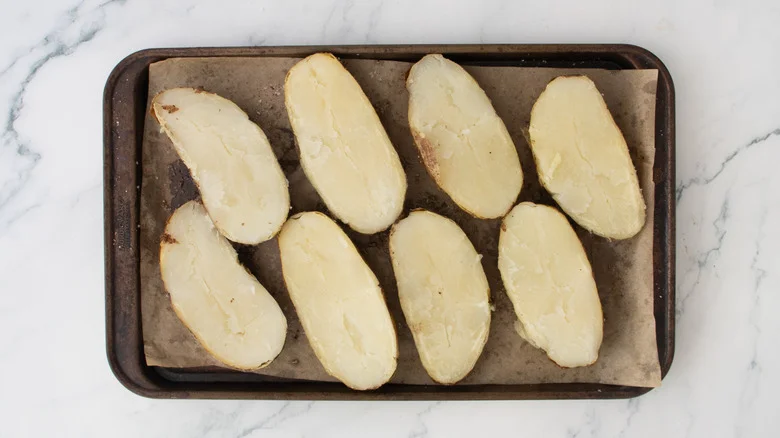 Four halved baked potatoes on a large baking sheet