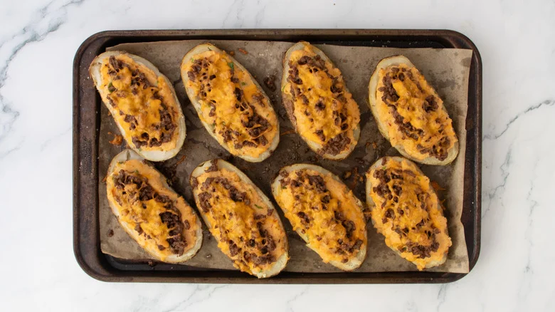Twice baked potatoes on a large baking sheet topped with cheese and taco beef