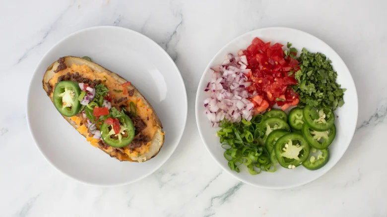 A plated taco-themed twice baked topped with tomatoes, jalapeños, onions, and herbs