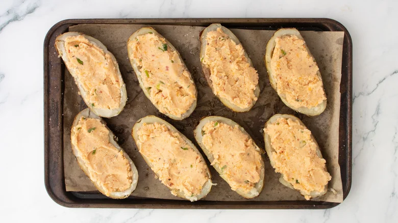Potato skins on a large baking sheet filled with seasoned mashed potato