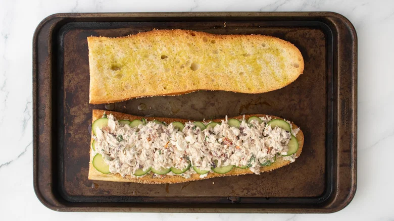 A layered tuna salad on a large toasted baguette.