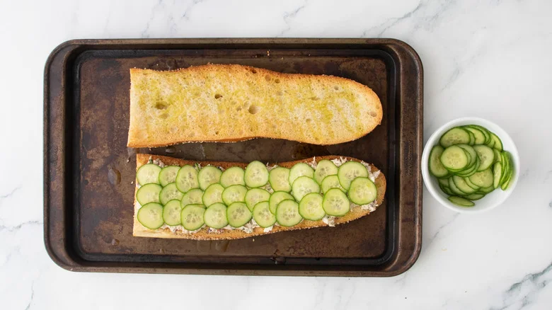 Tuna salad on a large toasted baguette topped with cucumber.